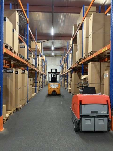 Vorkheftruck rijdt door het magazijn van RNDM Production tussen hoge stellingen met dozen
